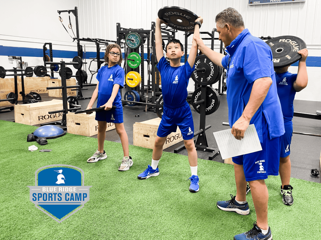 Boys lift weights in a gym while being instructed by a coach